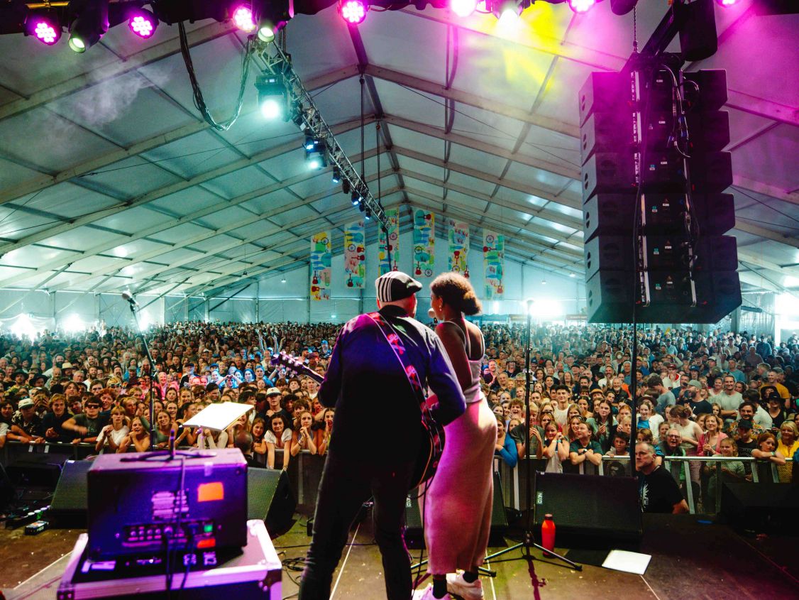 Man and woman singing into a microphone standing on a stage in front of a large audience.