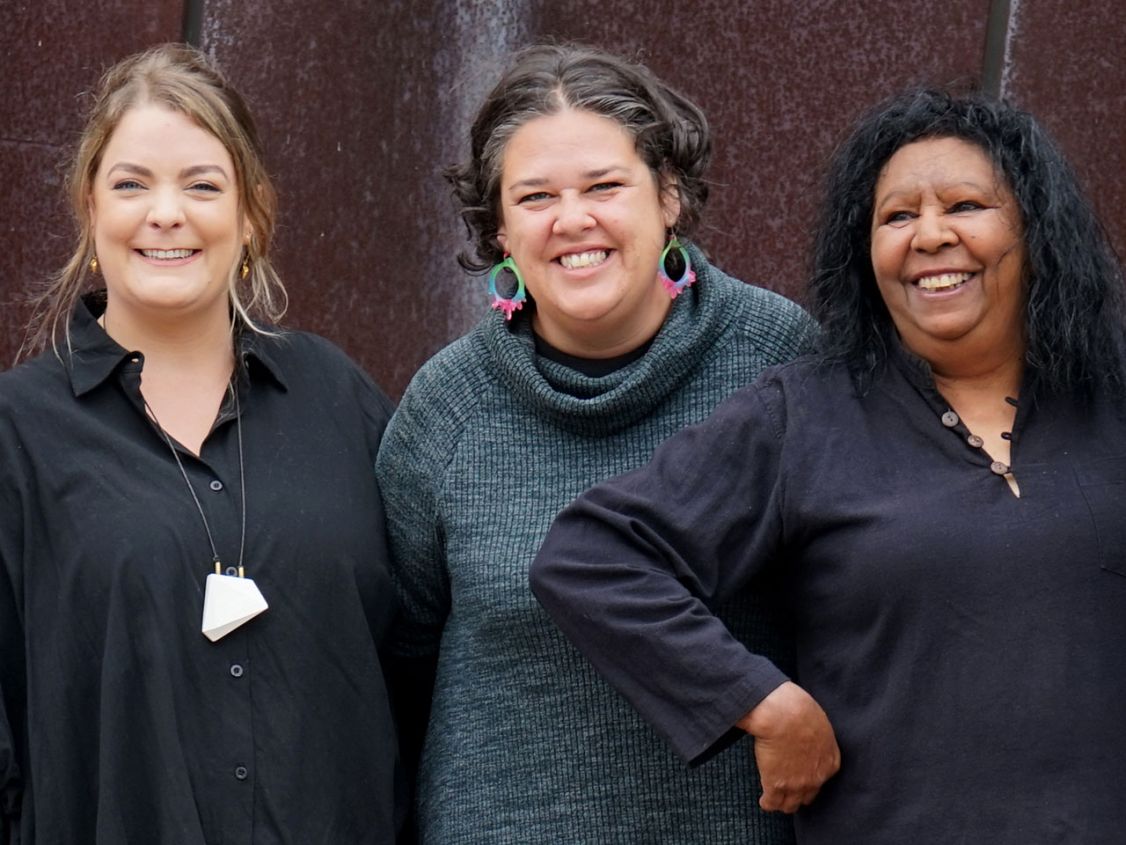 Three women in a row smiling at camera